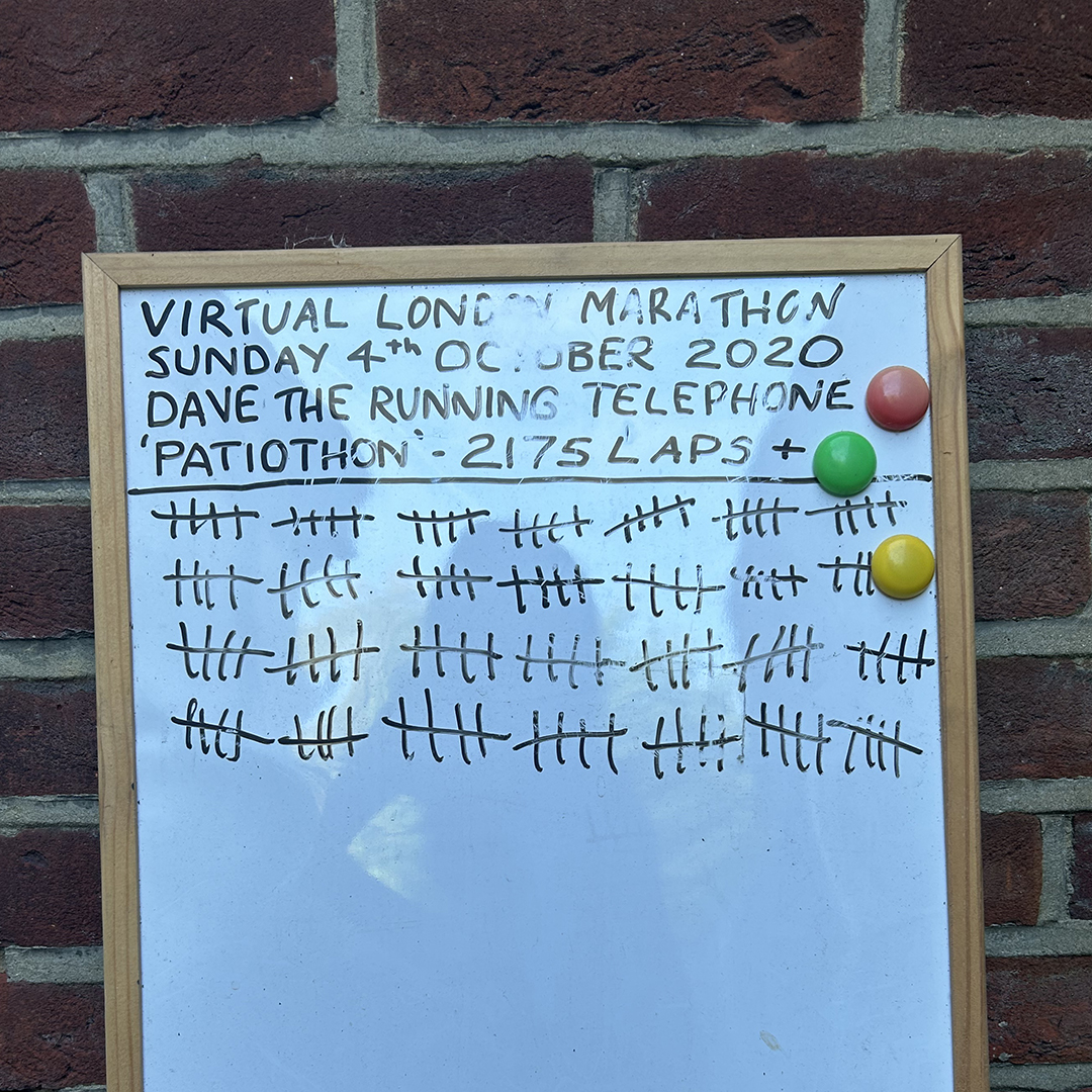 A white board with a lap tally leans against a brick wall.