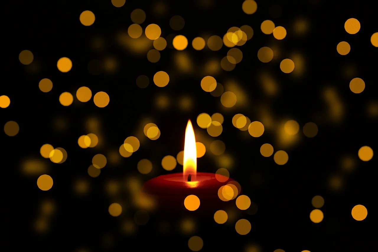 Close up of a lit candle. In the background are out of focus lights symbolizing other candles